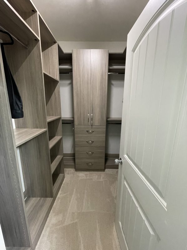 A spacious walk-in closet featuring a sizable mirror and a cabinet for storage.