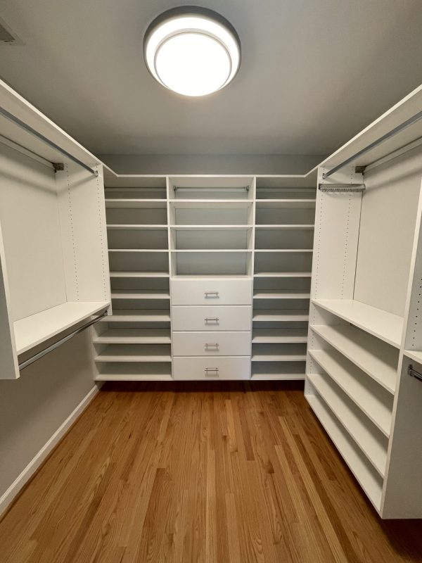 A walk-in closet with white cabinets and wooden floors, providing ample storage space and a stylish aesthetic.